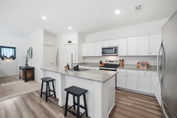 a kitchen with granite countertop a stove top oven a sink dishwasher a dining table and chairs with wooden floor