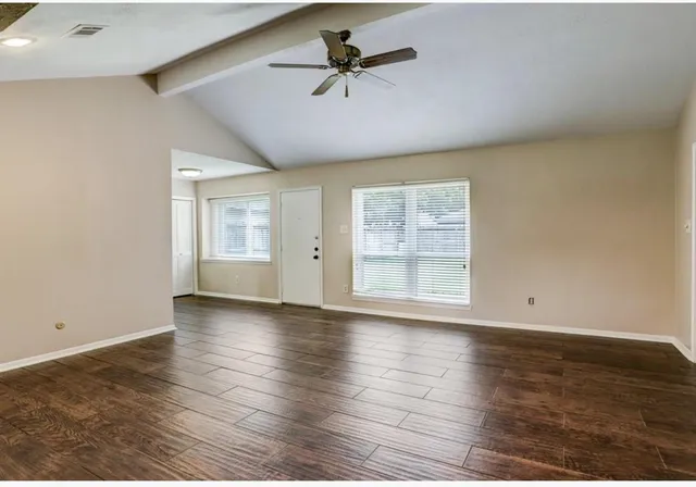 an empty room with wooden floor chandelier fan and windows
