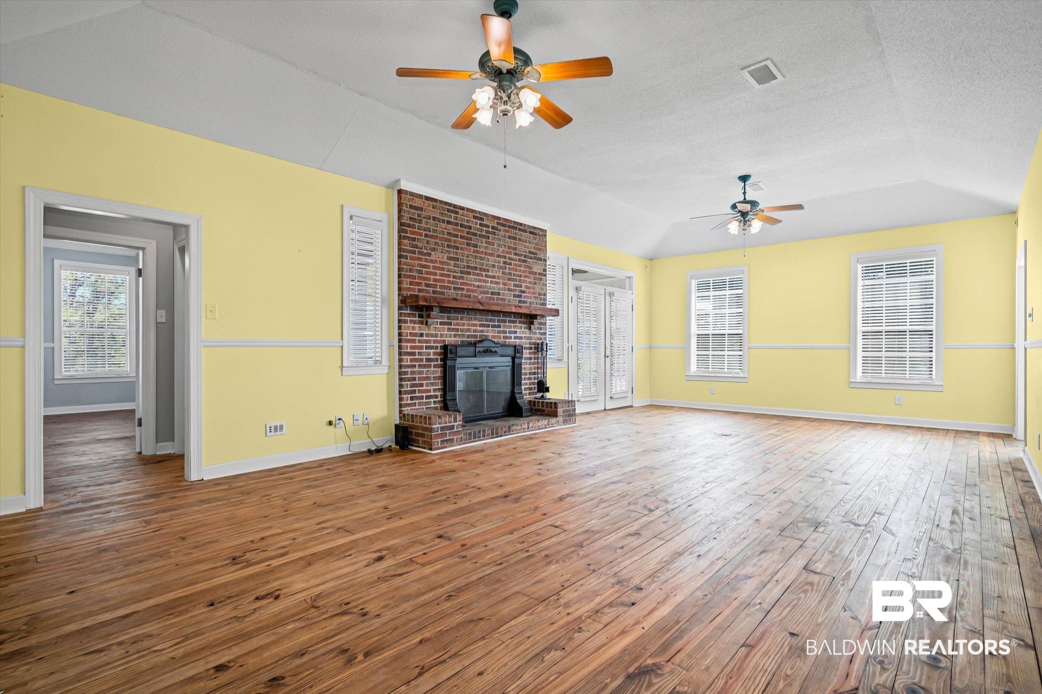 7650 Iron Rush Road Wilmer, AL 36587 - Photo 9 of 34 Unfurnished living room featuring vaulted ceiling, a fireplace, hardwood / wood-style flooring, a ceiling fan, and a textured ceiling