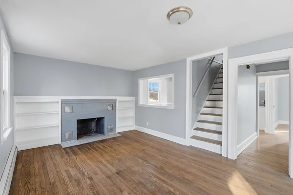 a view of an empty room with wooden floor fireplace and windows