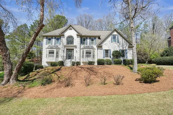 a view of a white house next to a yard with large trees