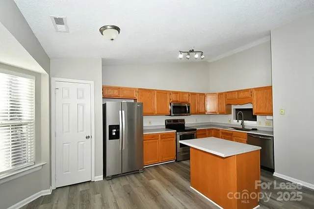 a kitchen with stainless steel appliances granite countertop a refrigerator a sink dishwasher a stove and a dining table with wooden floor