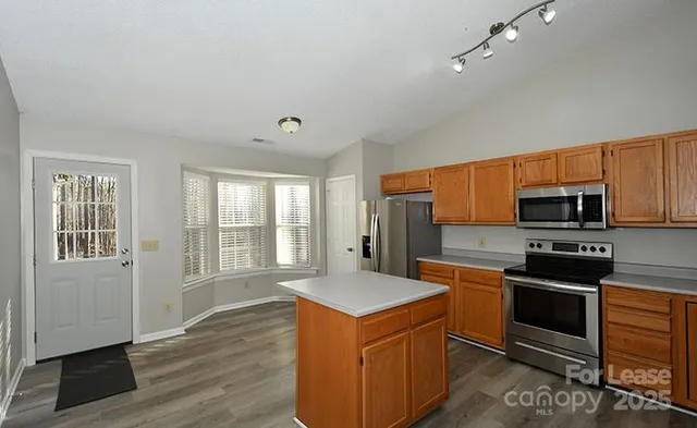 a kitchen with stainless steel appliances granite countertop a stove top oven a sink dishwasher a refrigerator and white cabinets with wooden floor