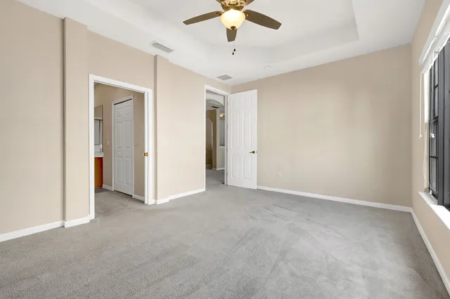 an empty room with chandelier fan and windows