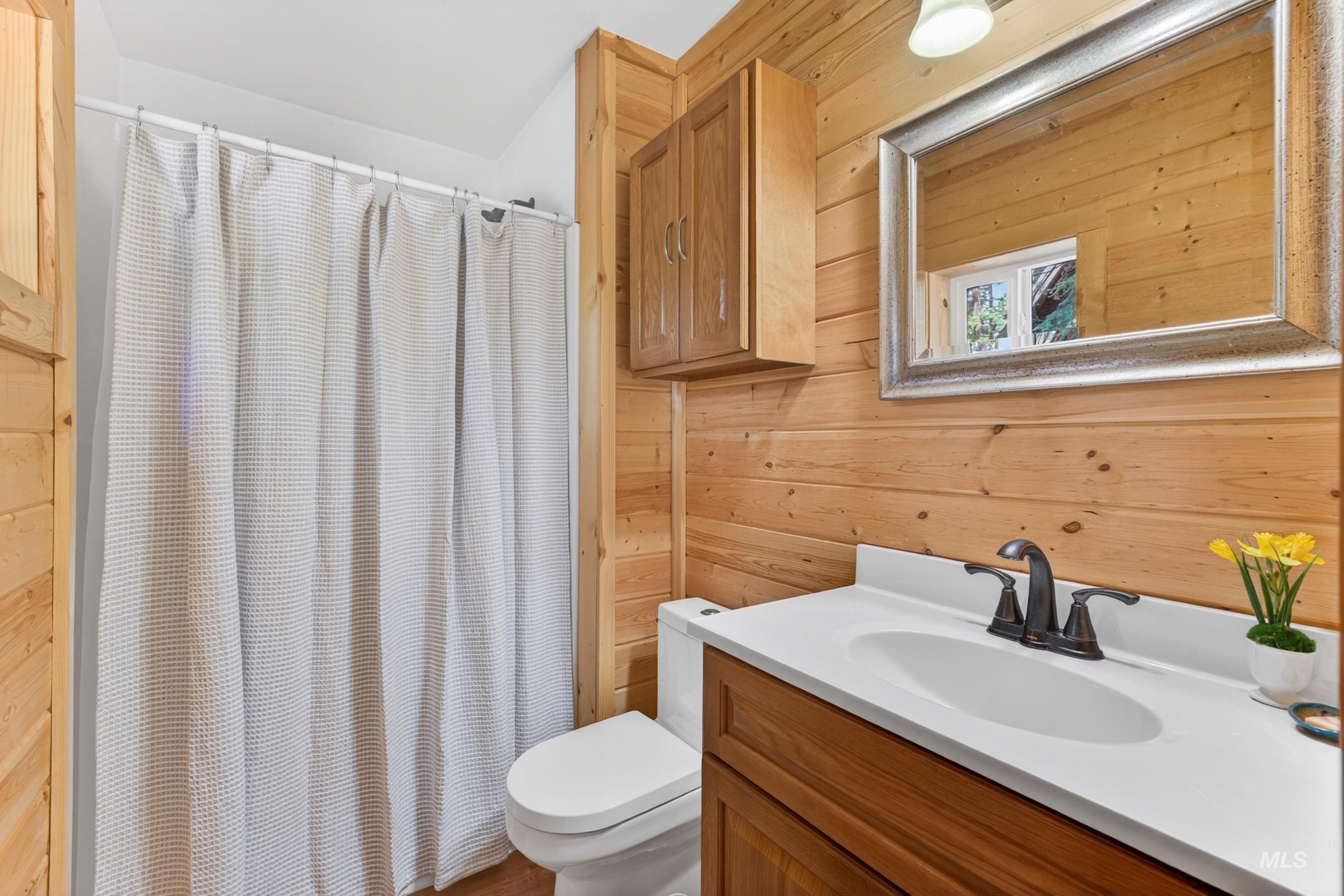 2339 West Mountain Road Donnelly, ID 83615 - Photo 17 of 37 Bathroom featuring plank wood-finish walls, a wood-finish vanity with a white countertop and integrated sink, a dark bronze-finish faucet, and a wall-mounted mirror with a decorative frame