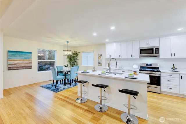 a kitchen with stainless steel appliances granite countertop a stove top oven a sink a dining table and chairs with wooden floor