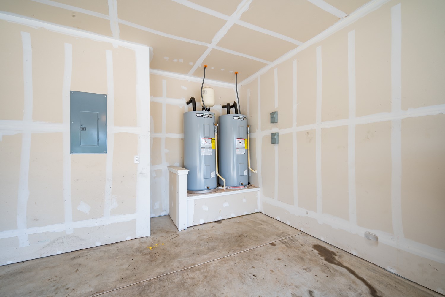 14917 Bajada Rd Manor Manor, TX 78653 - Photo 27 of 31 Utility area featuring two large water heaters on a raised platform, a wall-mounted electrical panel, exposed stud walls, and a concrete floor