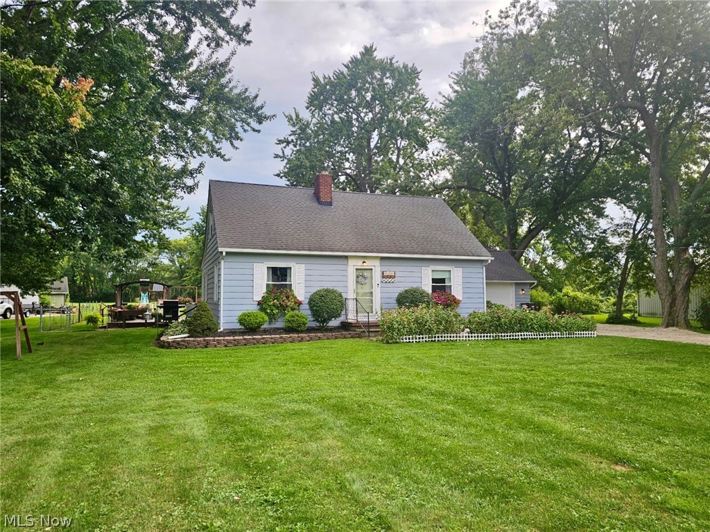 6620 West Lake Road Vermilion, OH 44089 - Photo 2 of 34 Classic Cape Cod cottage featuring a clean white exterior with dark roof accents, welcoming front entry with traditional shutters, and manicured landscaping including mature shade trees and foundational plantings