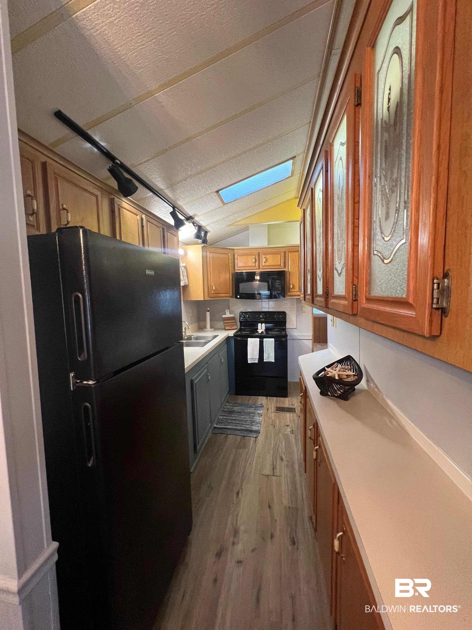 698 Escambia Loop Lillian, AL 36549 - Photo 8 of 16 Kitchen with sink, a textured ceiling, black appliances, lofted ceiling with skylight, and light hardwood / wood-style floors
