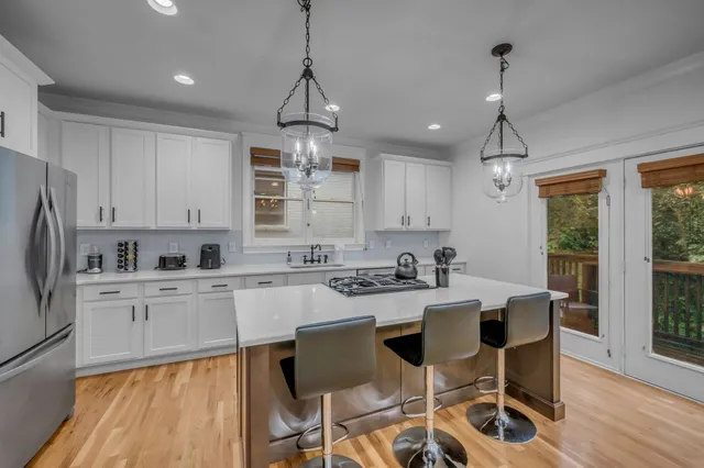 a kitchen with stainless steel appliances a stove a sink a refrigerator and white cabinets with wooden floor