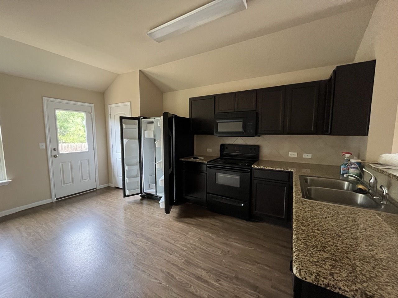 3510 Wickham Lane Austin, TX 78725 - Photo 12 of 16 Kitchen with black appliances, vaulted ceiling, dark wood-style flooring, dark cabinetry, and decorative backsplash
