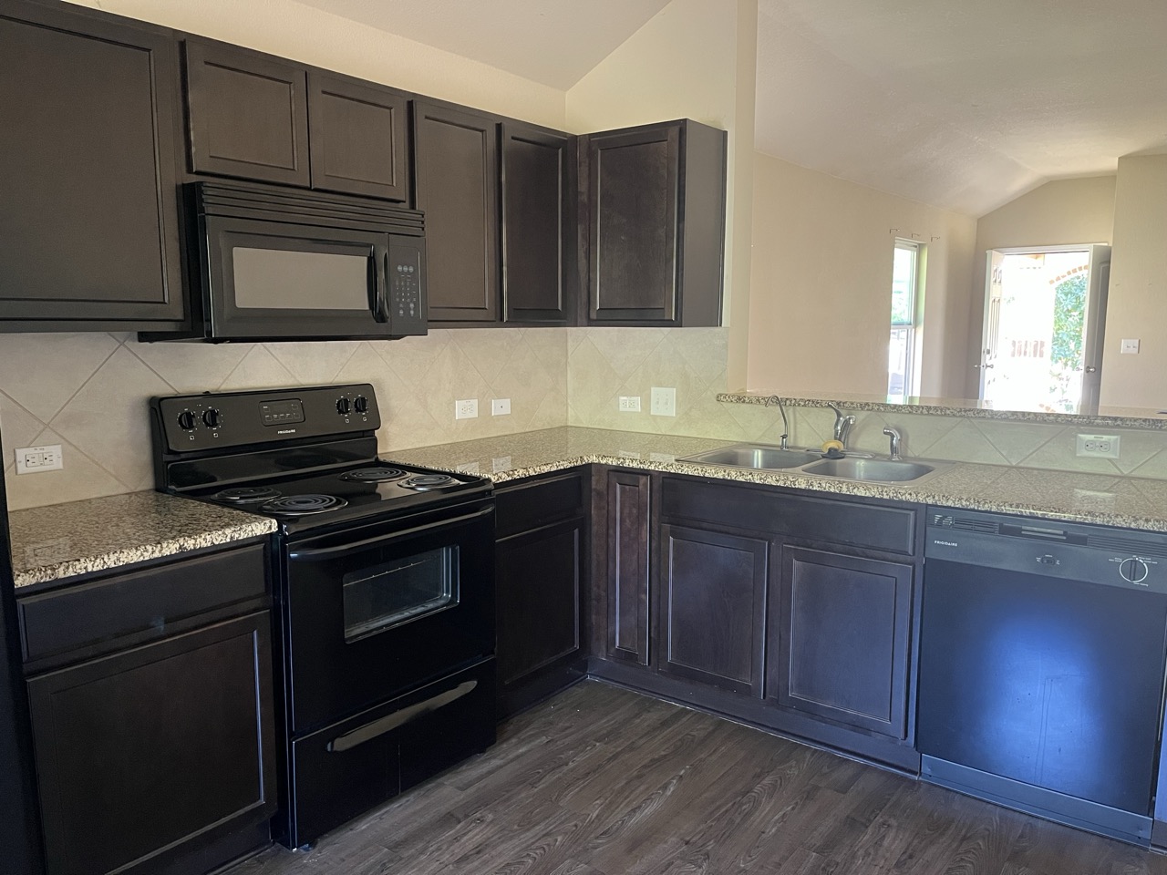 3510 Wickham Lane Austin, TX 78725 - Photo 7 of 16 Kitchen with black appliances, lofted ceiling, backsplash, light stone counters, and dark wood finished floors