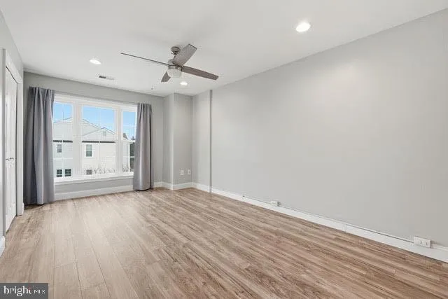 an empty room with wooden floor a ceiling fan and windows