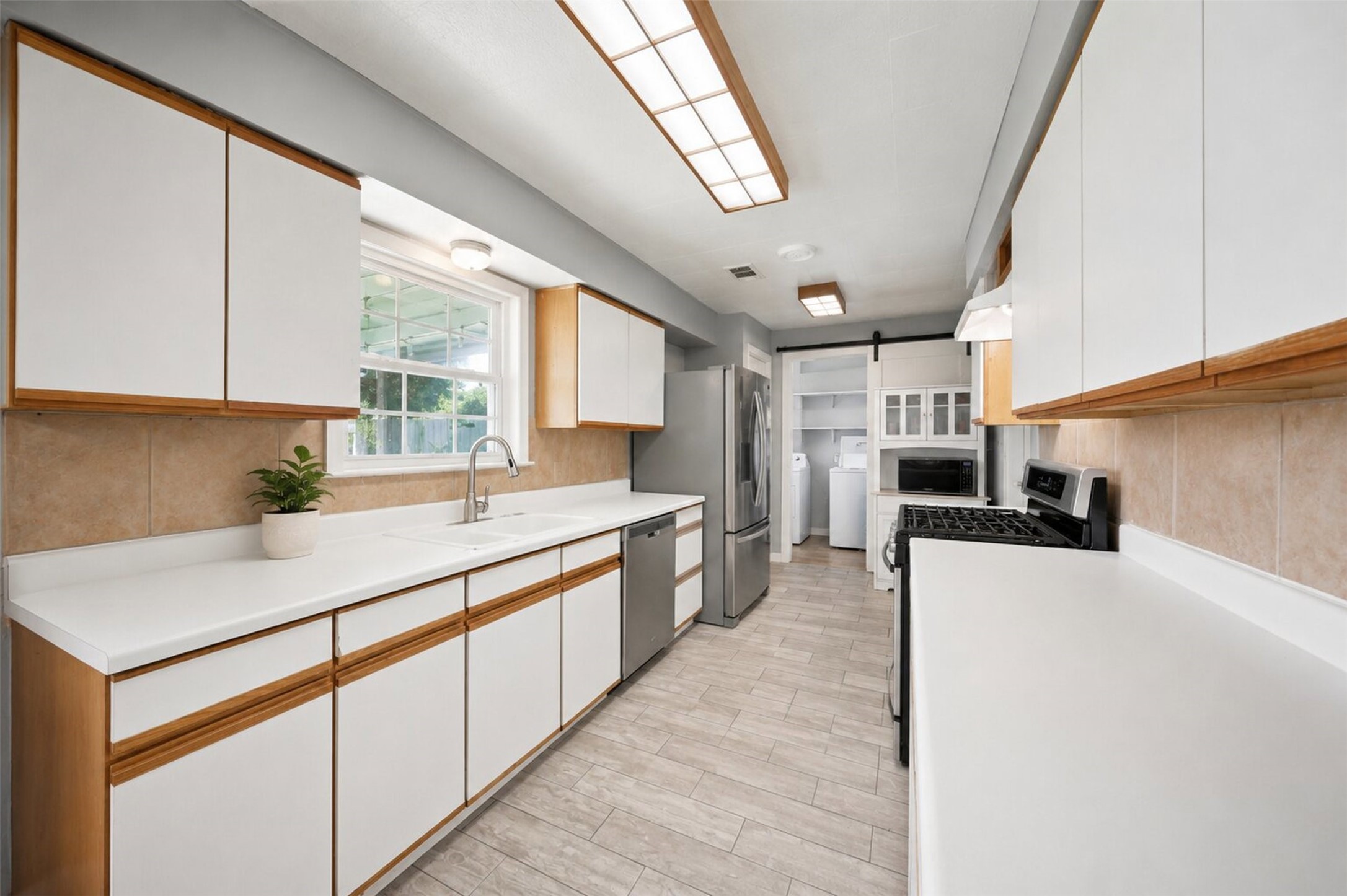 1306 Camden Road Pasadena, TX 77502 - Photo 5 of 16 Bright galley kitchen featuring white cabinetry, white laminate countertops, stainless steel appliances, and a view straight into the utility room, functional and full of storage!