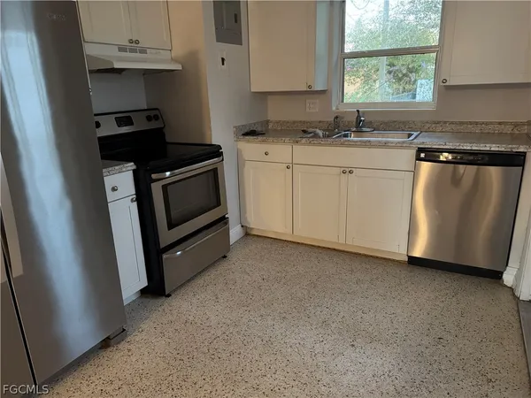 a kitchen with white cabinets a sink a stove and a window