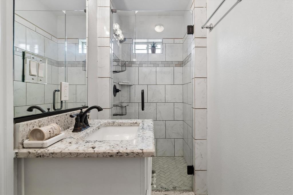 3007 McReynolds Road Sanger, TX 76266 - Photo 26 of 39 Bathroom featuring a granite countertop vanity with an undermount sink, bronze-finish faucet, and a tiled shower with a glass enclosure