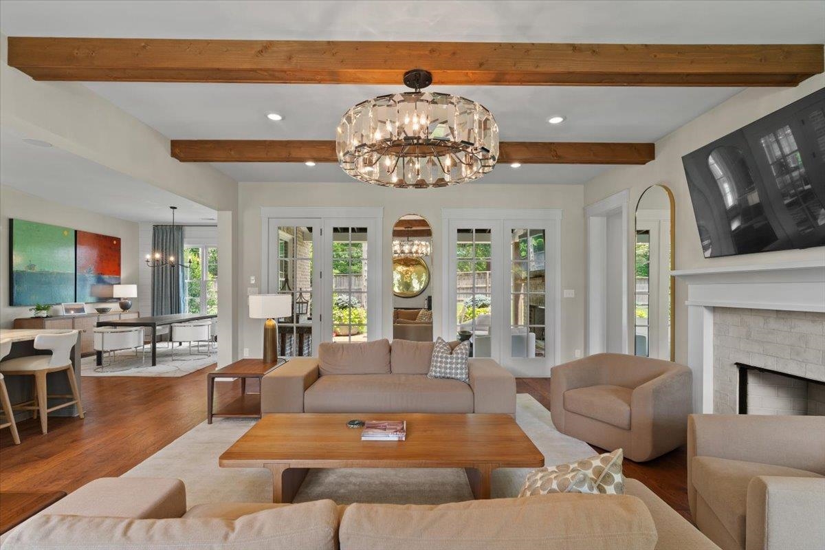 240 Burrows Road Collierville, TN 38017 - Photo 8 of 37 Living room featuring exposed wood beams, a contemporary chandelier, a fireplace with a stone surround and mantel, double French doors, and wood-finish flooring