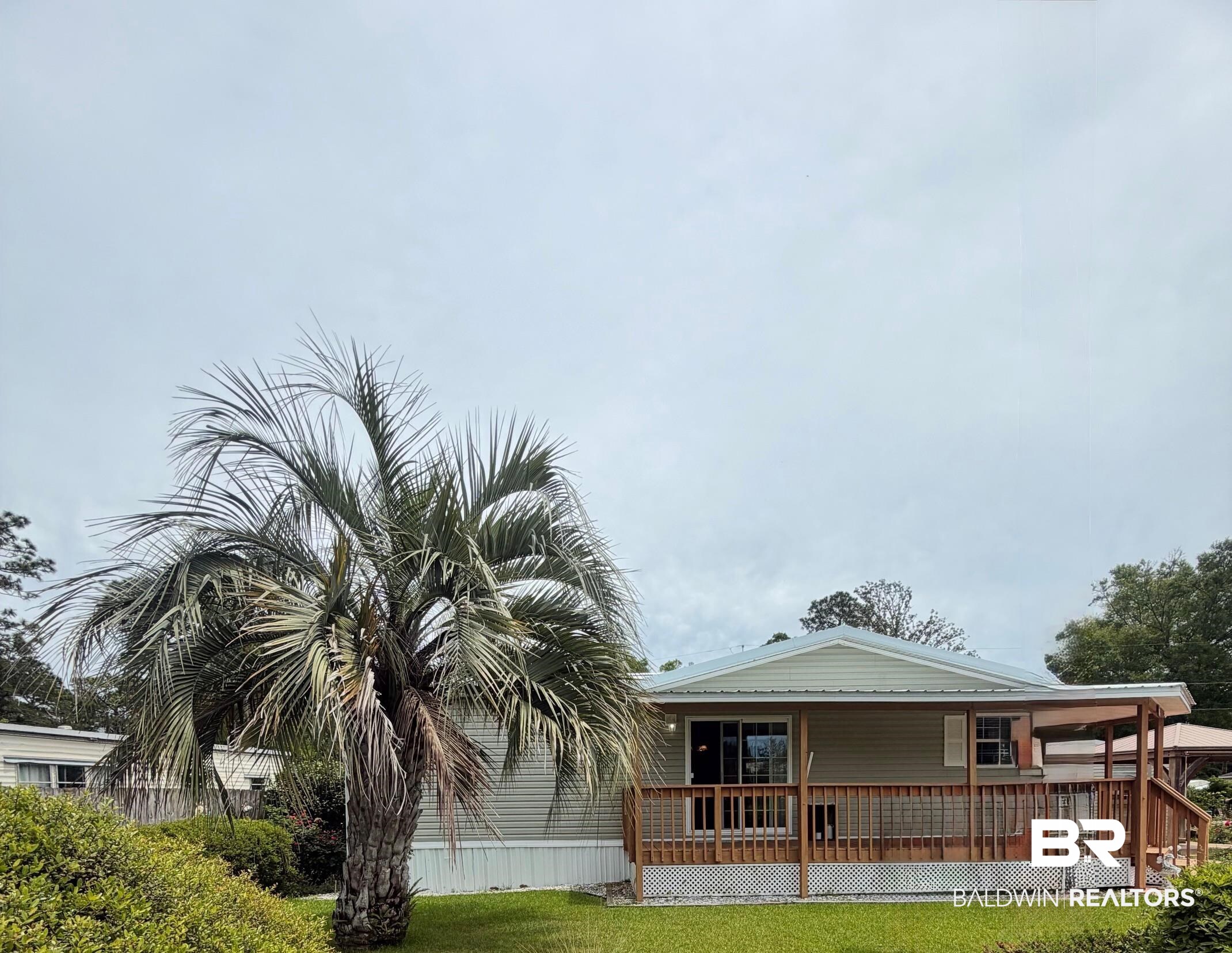 675 Escambia Loop Lillian, AL 36549 - Photo 1 of 44 Exterior with light-colored siding, a wood deck with lattice skirting, and a prominent palm tree