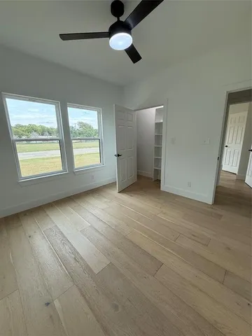 an empty room with wooden floor fan and windows