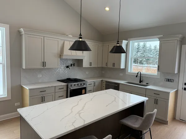 a kitchen with stainless steel appliances a sink a stove a refrigerator white cabinets and wooden floor