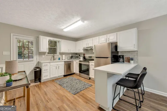 a kitchen with a refrigerator a stove top oven a sink dishwasher and white cabinets with wooden floor