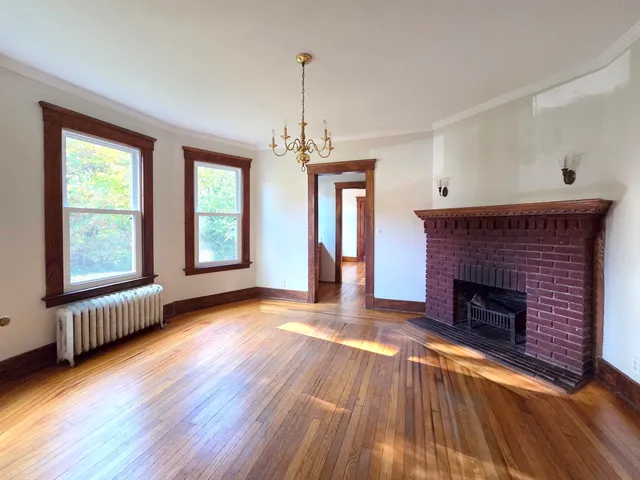 a view of an empty room with wooden floor fireplace and a window