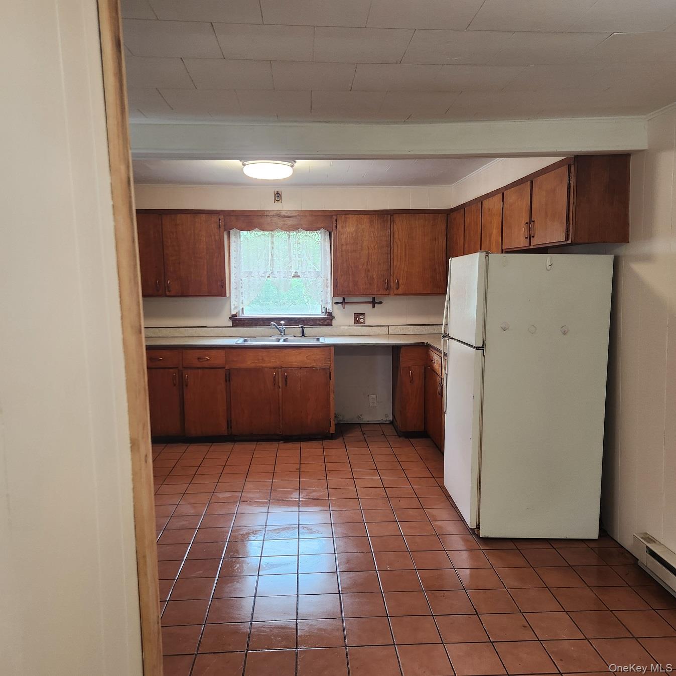 476 Old Rte 17 Livingston Manor, NY 12758 - Photo 4 of 39 Kitchen featuring freestanding refrigerator, baseboard heating, light countertops, brown cabinetry, and light tile patterned flooring