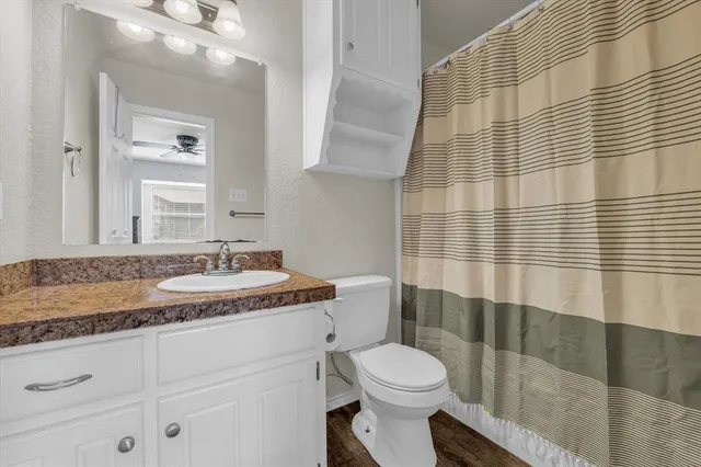 a bathroom with a granite countertop sink toilet a mirror and shower curtain