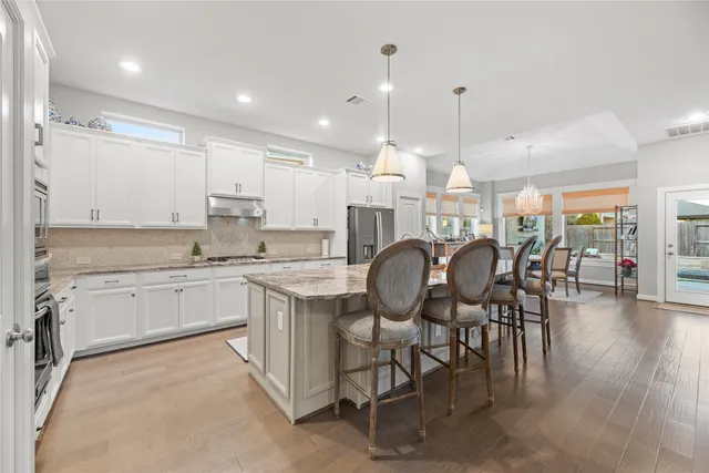 a large kitchen with kitchen island granite countertop lots of white cabinets appliances and dining table