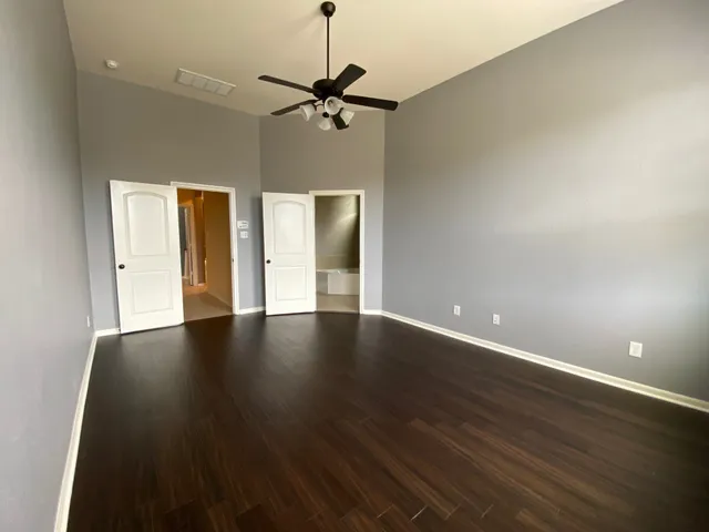 a view of an empty room with wooden floor and a ceiling fan