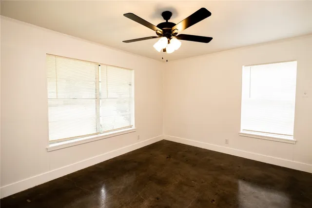 an empty room with wooden floor fan and windows