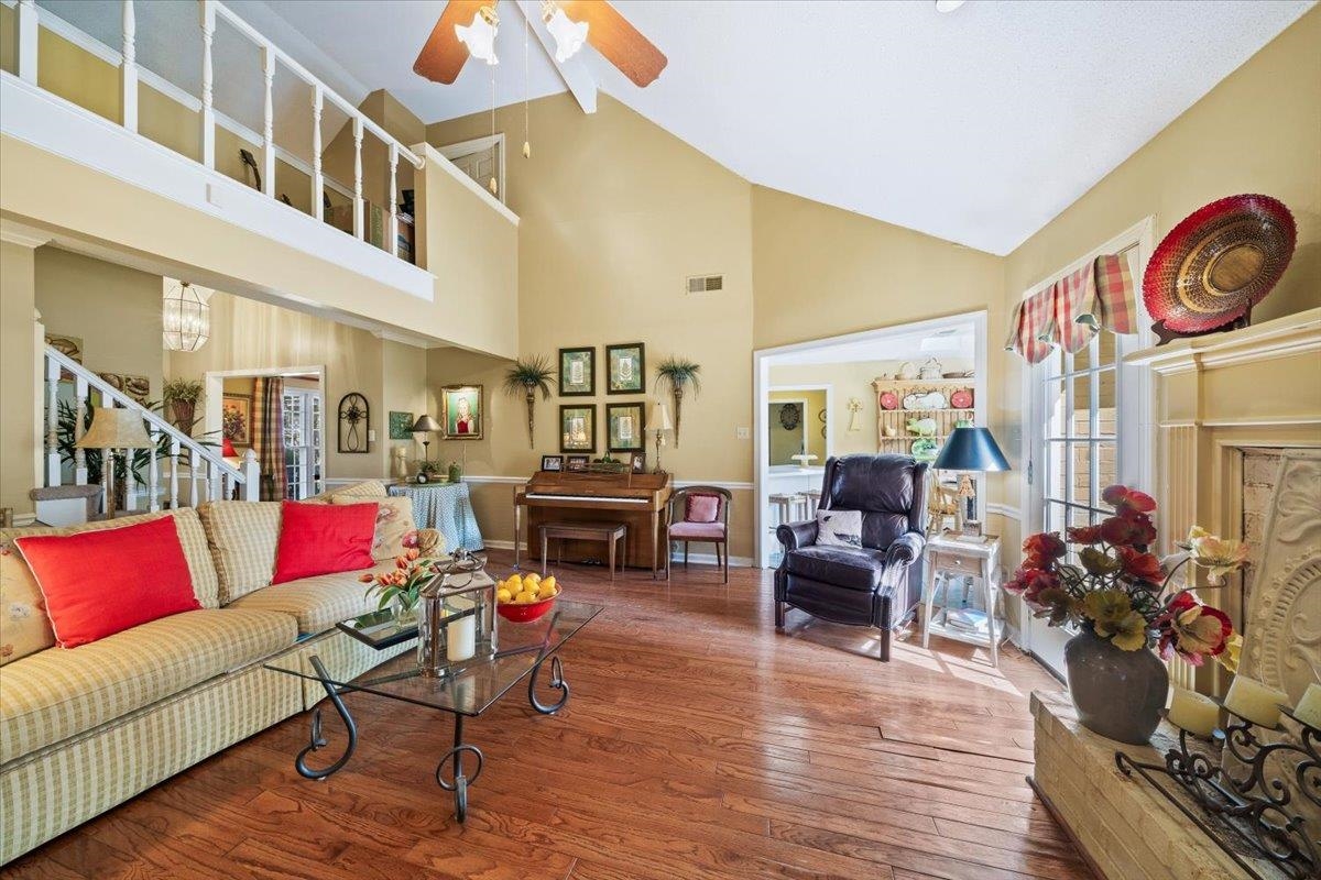 Living room with hardwood / wood-style flooring, high vaulted ceiling, a ceiling fan, and stairs