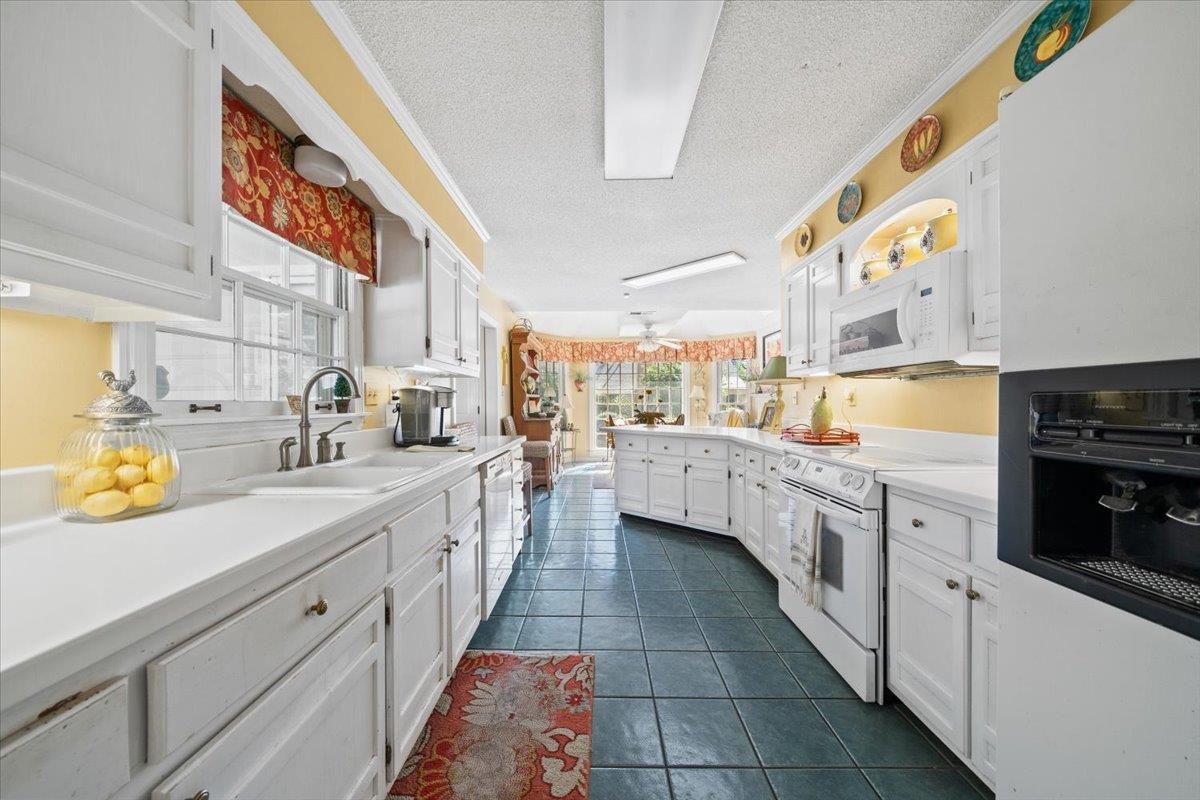 Kitchen featuring white cabinetry, white appliances, healthy amount of natural light, a textured ceiling, and light countertops
