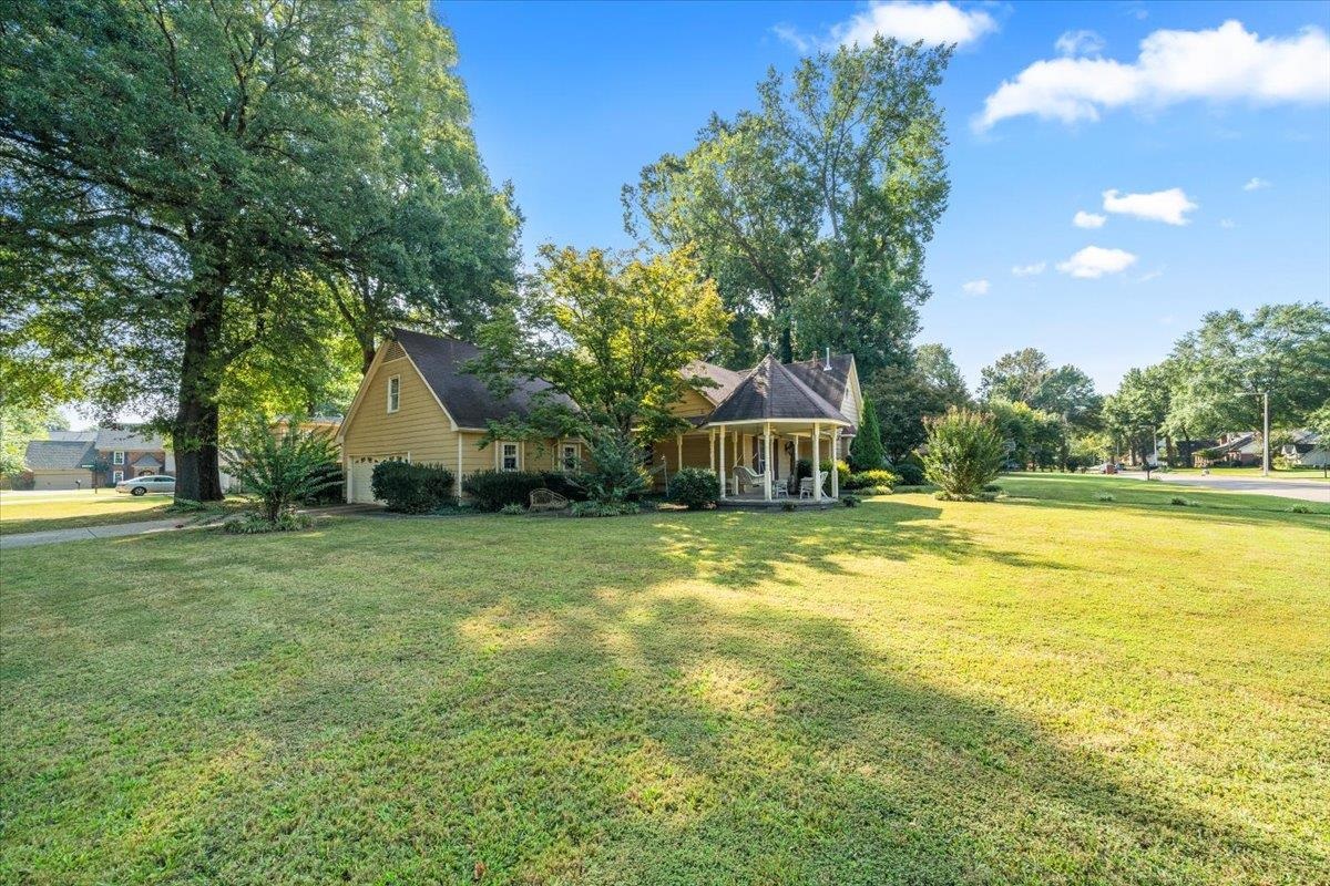 View of green lawn featuring a porch and a garage