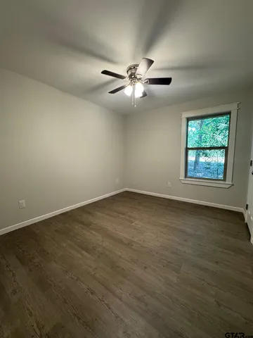 an empty room with wooden floor ceiling fan and windows