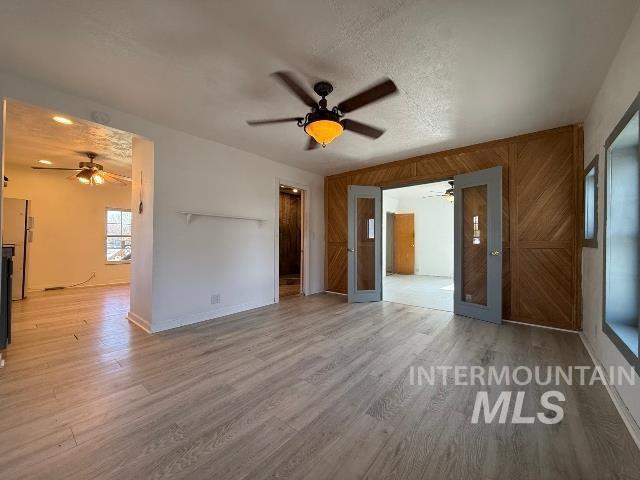 902 East Main Street Weiser, ID 83672 - Photo 2 of 45 Unfurnished living room featuring a ceiling fan, light wood-style flooring, wooden walls, and a textured ceiling
