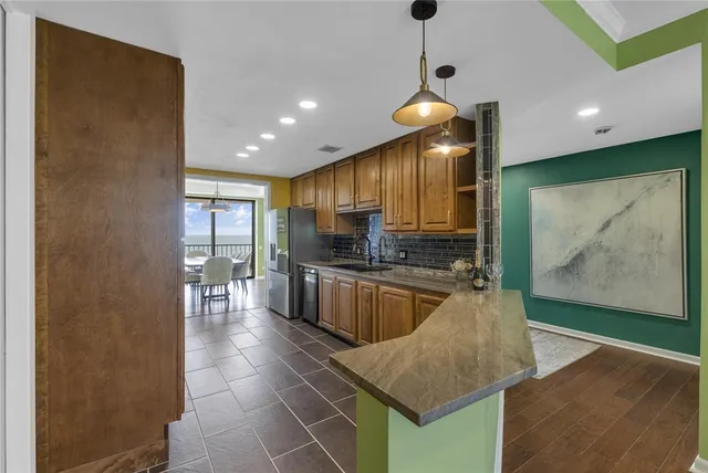 a kitchen with stainless steel appliances granite countertop wooden cabinets a sink dishwasher a stove and a refrigerator with wooden floor