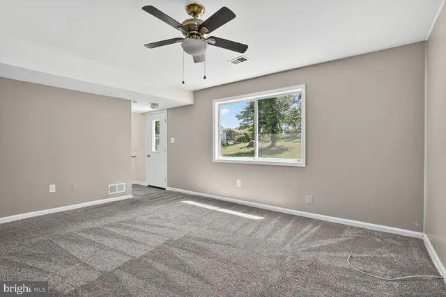 an empty room with ceiling fan and windows