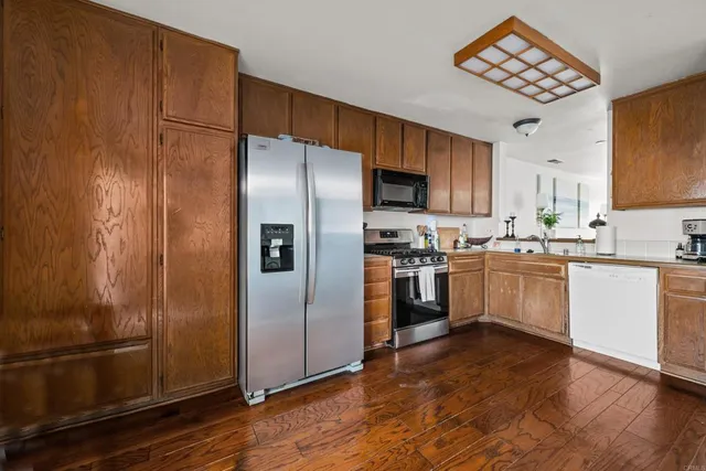 a kitchen with a refrigerator stainless steel appliances wooden floor and a window