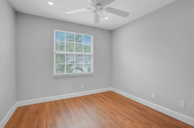 an empty room with wooden floor chandelier fan and windows