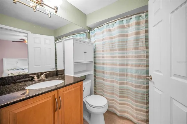 a bathroom with a granite countertop sink a toilet a mirror and shower curtain