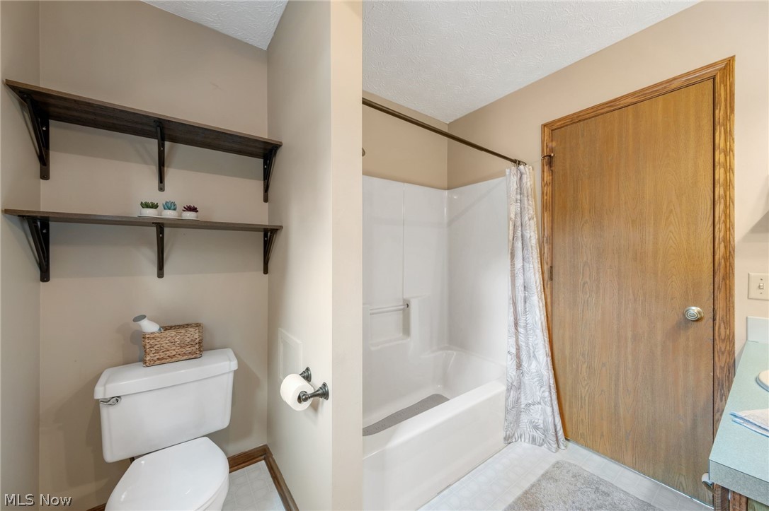 2140 Pickle Road Akron, OH 44312 - Photo 23 of 30 Bathroom featuring tile patterned flooring, shower / bathtub combination with curtain, toilet, and a textured ceiling