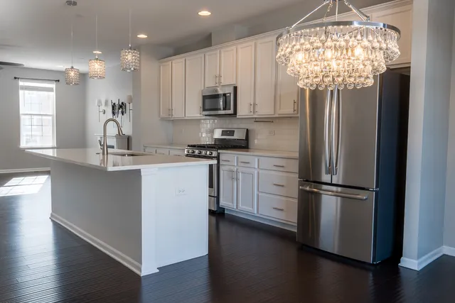 a open kitchen with stainless steel appliances granite countertop a stove a sink a refrigerator and white cabinets with wooden floor