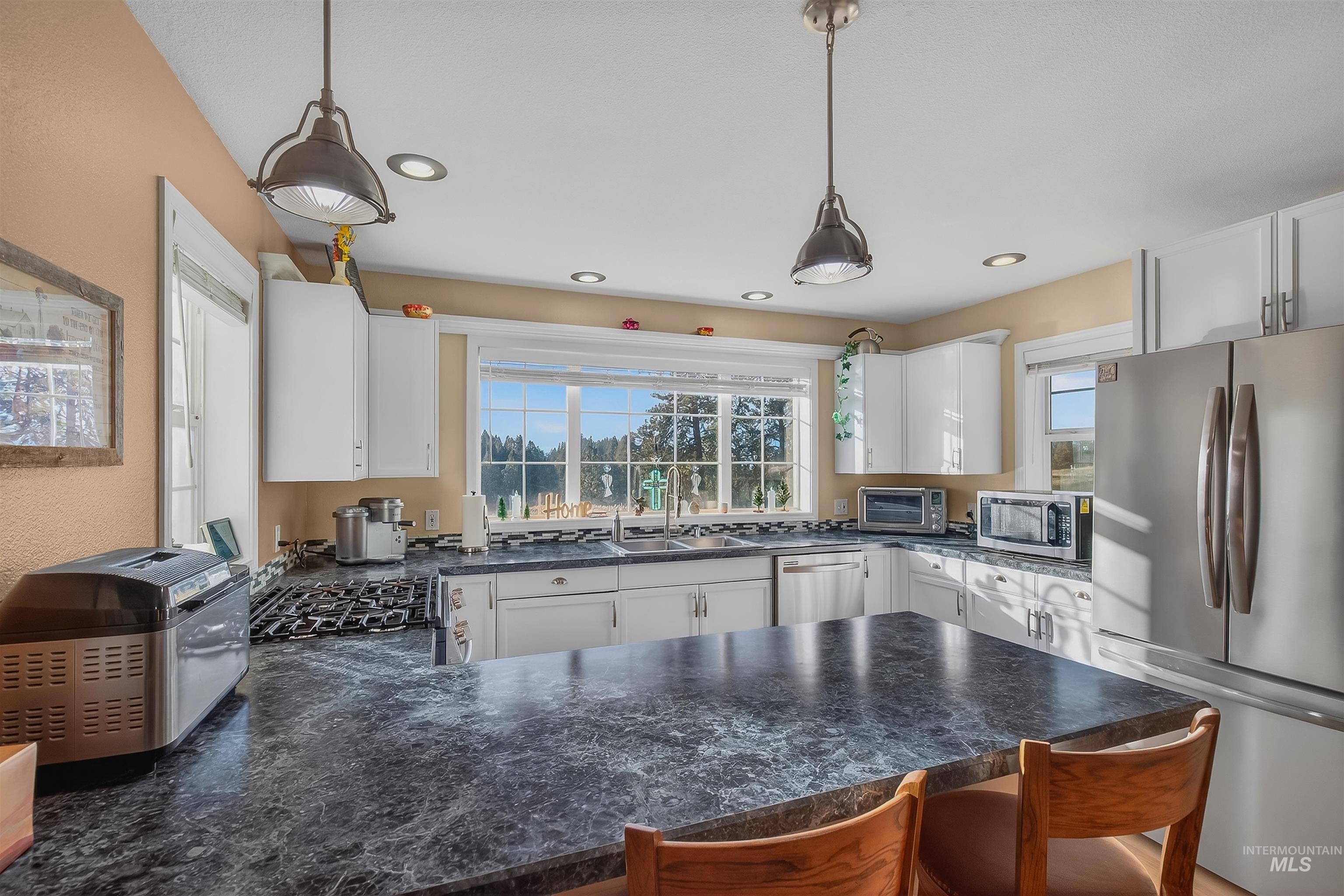 108 Tweedy Lane Kooskia, ID 83539 - Photo 26 of 48 Kitchen with stainless steel appliances, a peninsula, a breakfast bar area, white cabinetry, and hanging light fixtures
