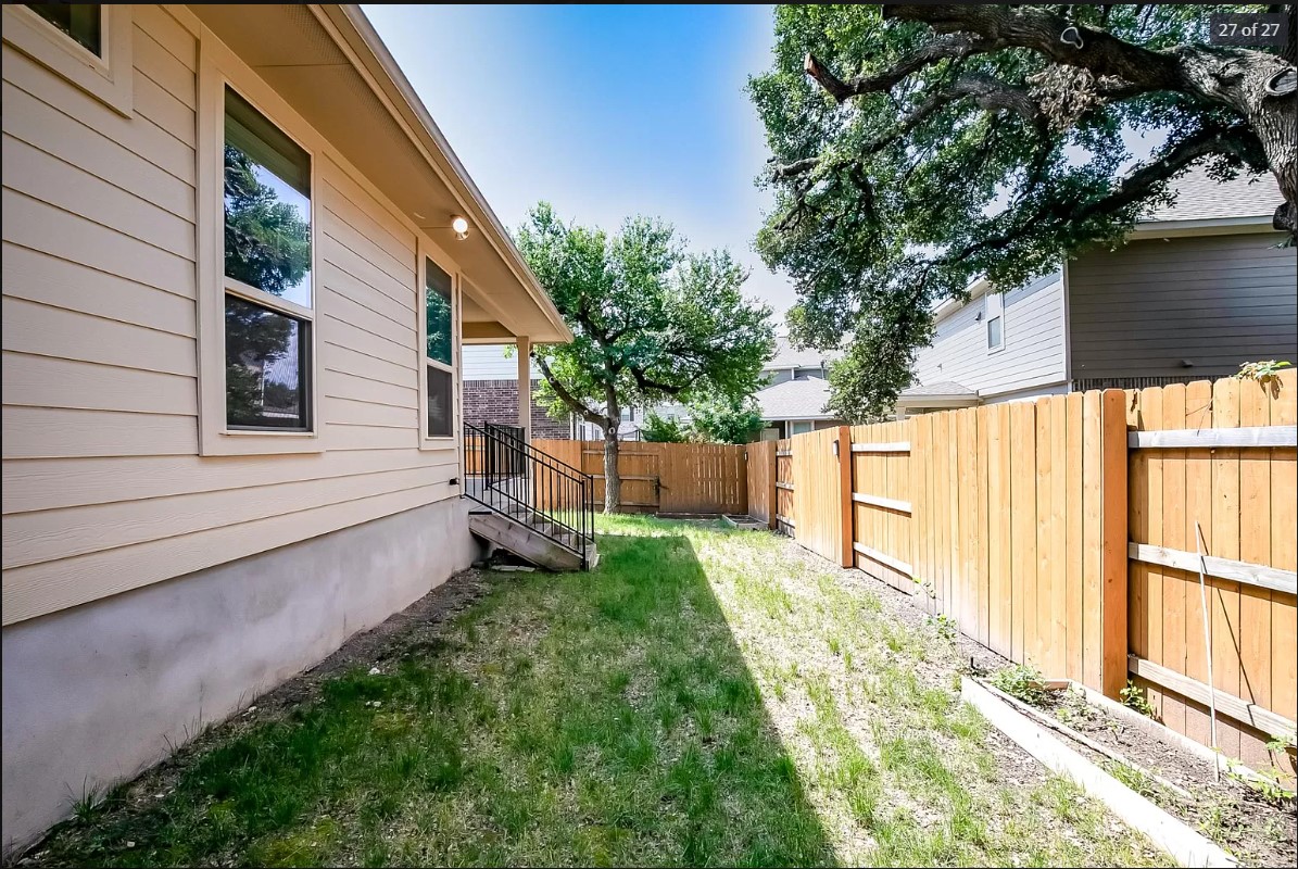 14215 McCoy Loop Austin, TX 78717 - Photo 25 of 27 Expansive side yard featuring a partial wood privacy fence, concrete foundation, and a rear entrance with metal railings