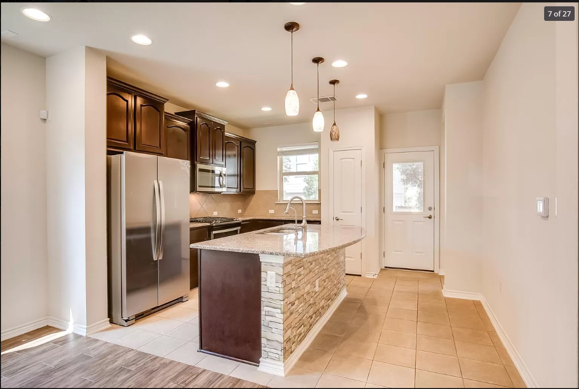 14215 McCoy Loop Austin, TX 78717 - Photo 4 of 27 Kitchen with dark wood cabinetry, stainless steel appliances, a curved island featuring a stacked stone facade and granite countertop, and recessed lighting