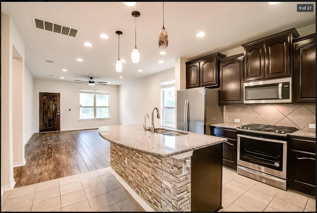14215 McCoy Loop Austin, TX 78717 - Photo 6 of 27 Open-concept kitchen featuring an island with a stacked stone facade and granite countertop, dark wood cabinetry, stainless steel appliances, and tile flooring