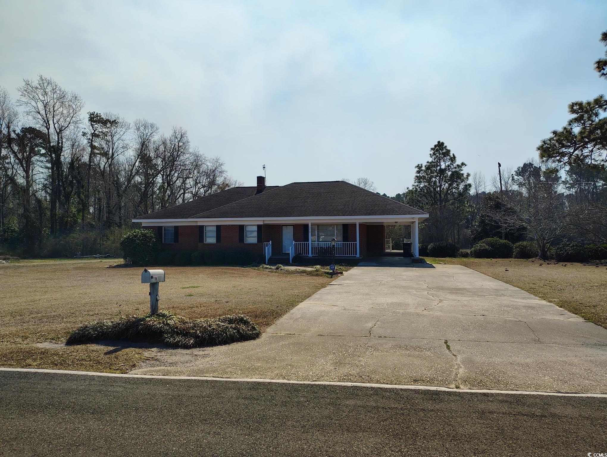 View of front of property featuring concrete driveway, a porch, a front lawn, and an attached carport