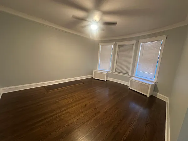 an empty room with wooden floor fan and windows