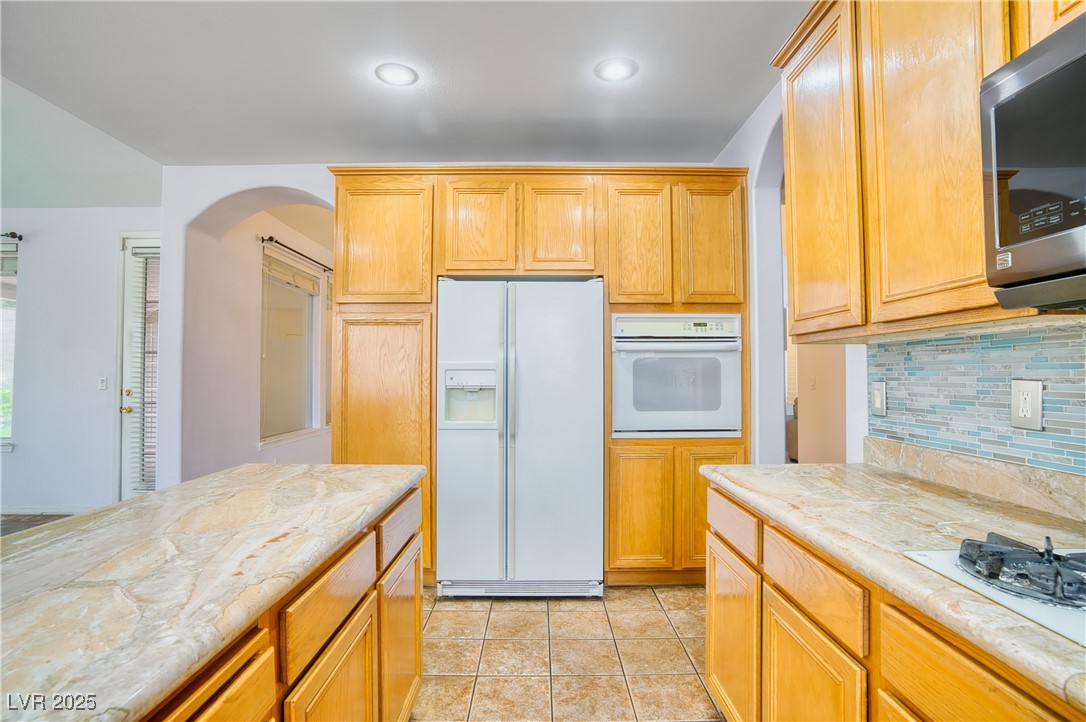 2383 Rainswept Avenue Henderson, NV 89052 - Photo 20 of 62 Kitchen featuring white appliances, backsplash, light tile patterned flooring, light stone countertops, and arched walkways